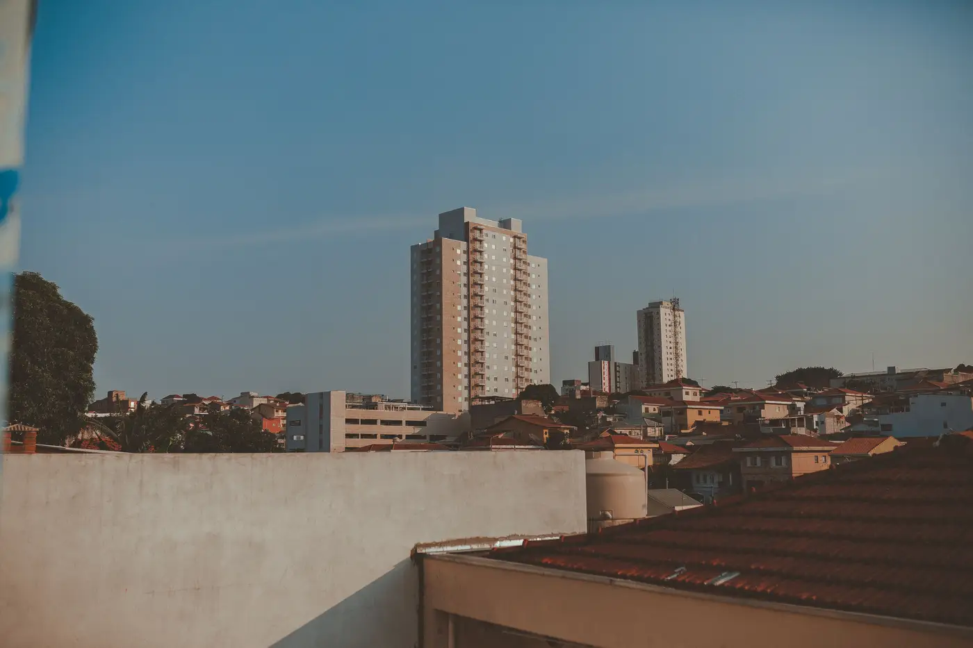 A city skyline at dusk with a tall residential high-rise and surrounding low rooftops.