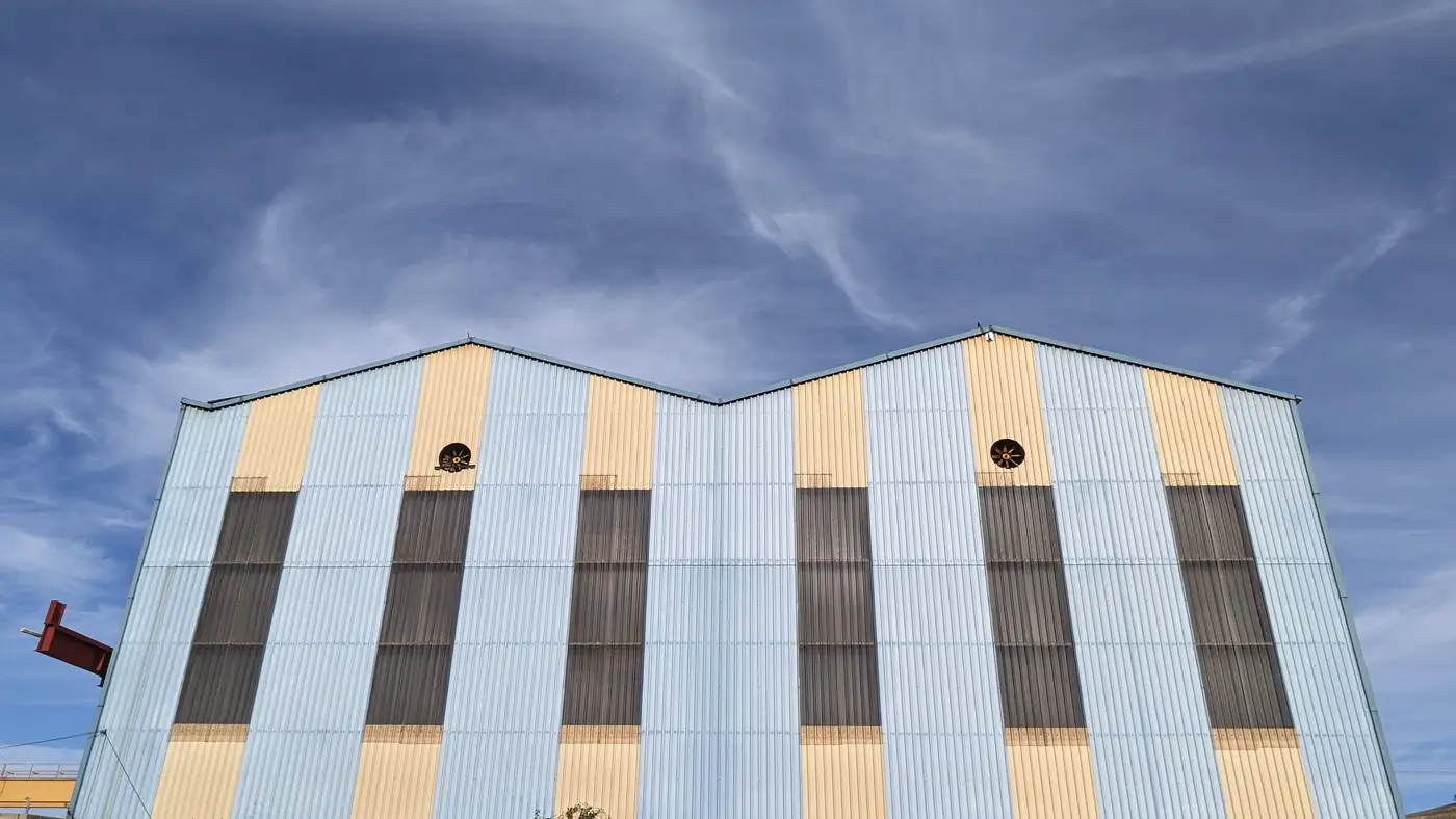 A pastel blue and cream gable-roofed warehouse building exterior under a clear sky.